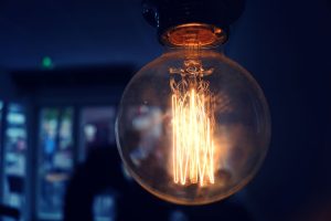 INICIO Close-up of a glowing vintage Edison light bulb in a dim indoor setting.