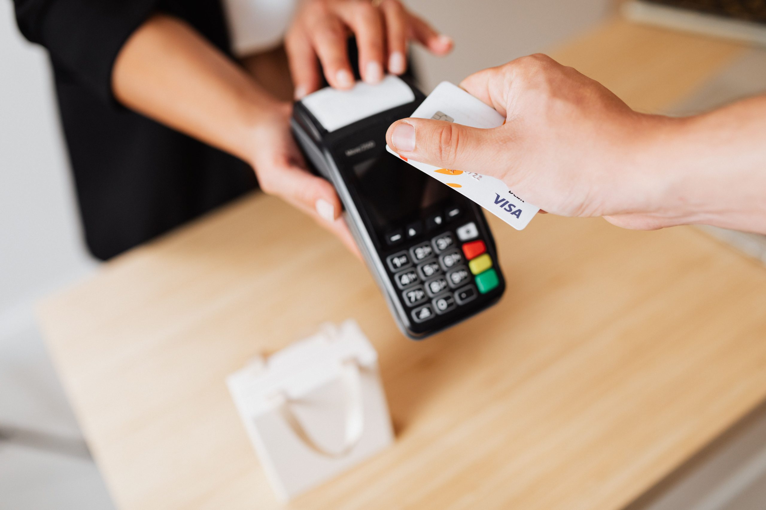 INICIO Close-up of hands using a contactless payment terminal with a credit card indoors.